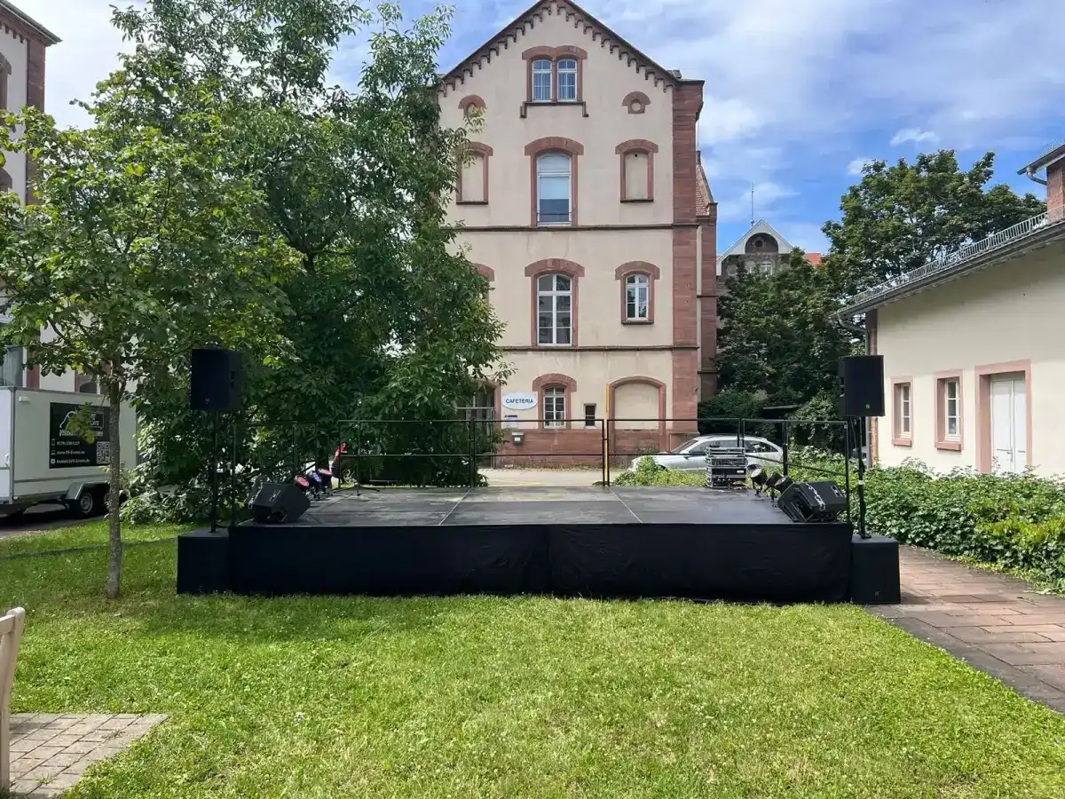 Schwarzes Bühnenpodest auf einer Wiese vor einem Gebäude
